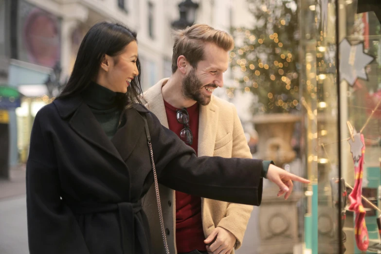 a man and a woman looking at a window display, pexels contest winner, pointing, people outside walk, flirting smiling, holiday