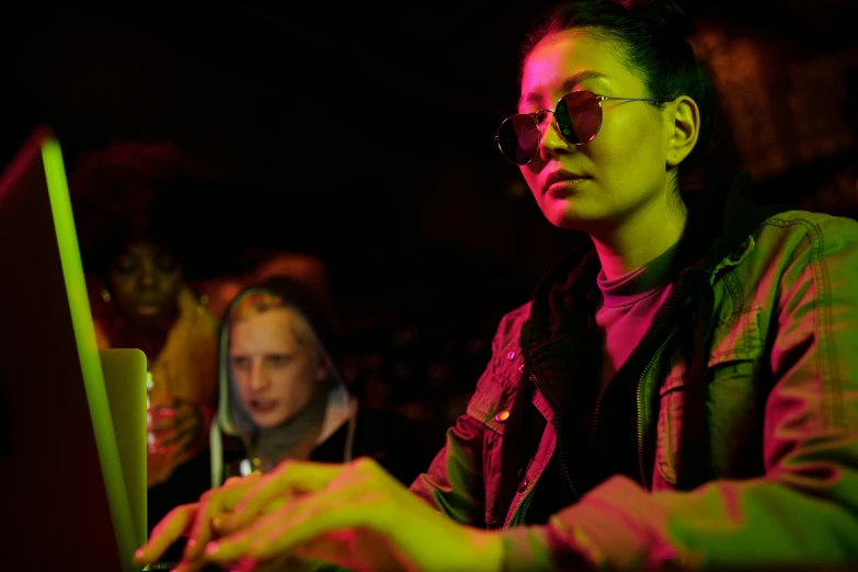 a woman sitting in front of a laptop computer, inspired by Liam Wong, photograph of three ravers, 7 0 mm. dramatic lighting, worksafe. cinematic, wearing gold glasses