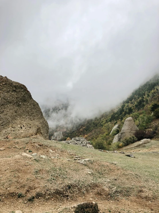 a red fire hydrant sitting on top of a lush green hillside, by Muggur, les nabis, light grey mist, boulders, dust clouds, inside a gorge