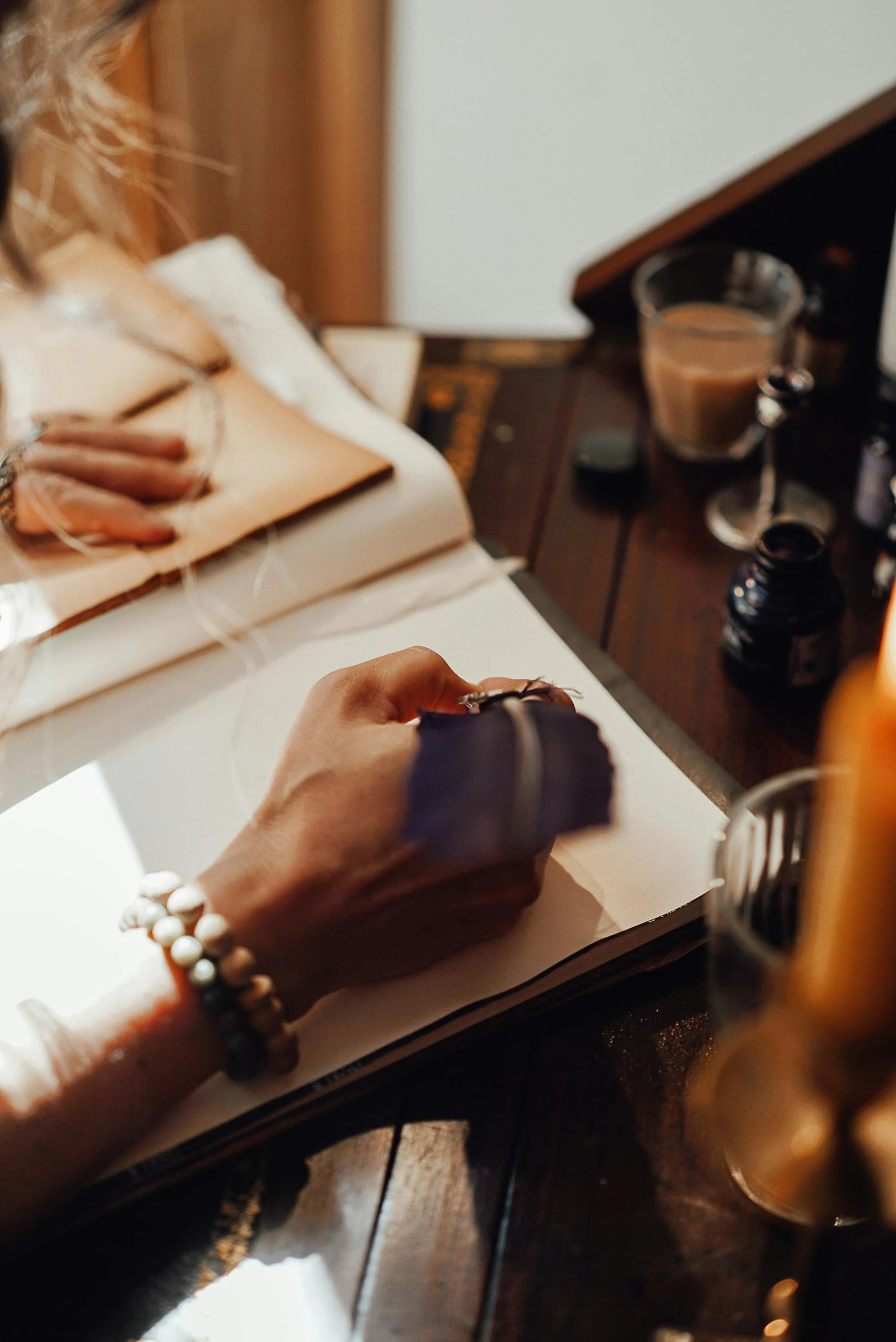 a woman sitting at a table writing on a piece of paper, trending on pexels, visual art, magical potions, leather jewelry, morning hard light, holding a book