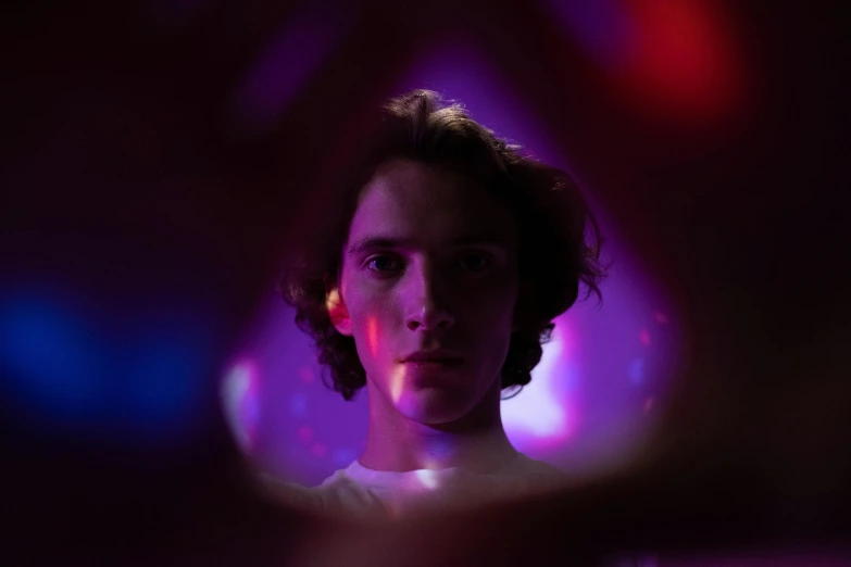 a woman looking at her reflection in a mirror, a character portrait, pexels contest winner, purple lights, teenage boy, promotional image, portrait of timothee chalamet