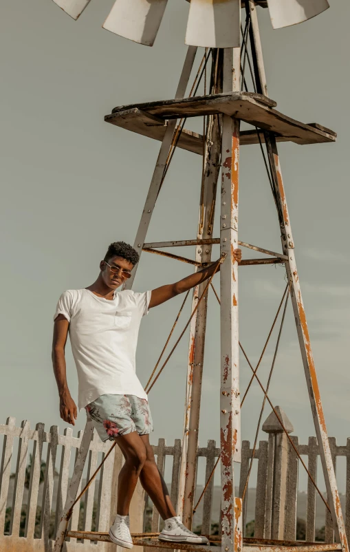a man standing in front of a windmill, an album cover, pexels contest winner, tan skin a tee shirt and shorts, on stilts, jayison devadas, while smiling for a photograph