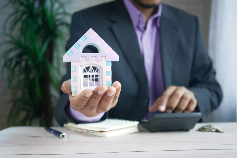 a man in a suit holding a model of a house, a cartoon, unsplash, pastel', coloured, black house, hand on table