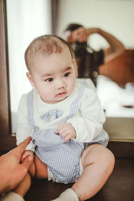 a baby sitting on the floor in front of a mirror, bao pham, bashful expression, blue overalls, detail shot