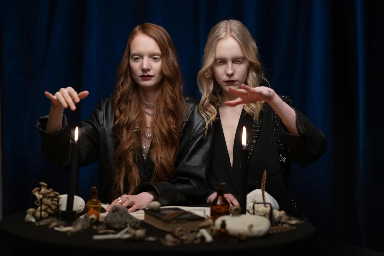 two women sitting at a table with candles, trending on pexels, surrealism, wearing black wizard robes, sophie turner, skulls in hands, studio photo