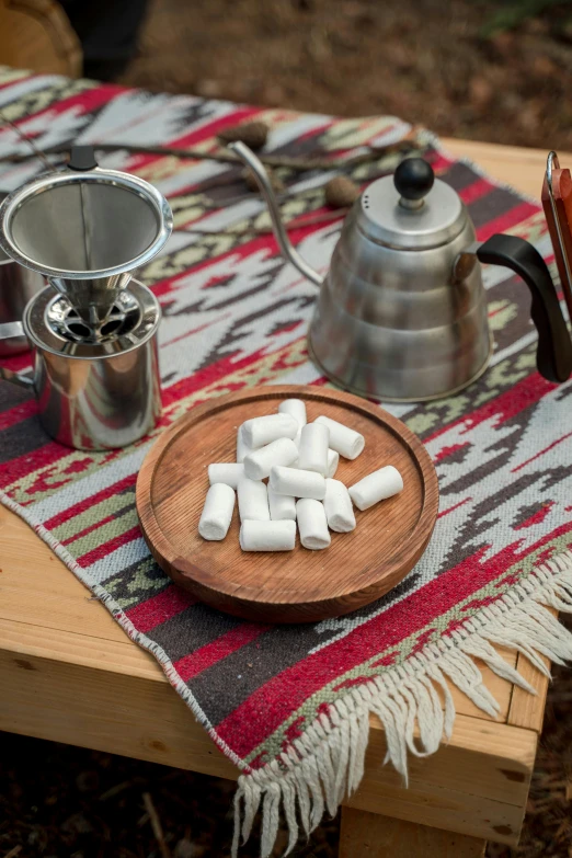 a wooden table topped with a plate of marshmallows, inspired by Ödön Márffy, unsplash, smokey cannons, tribal yurta, flasks, arabica style