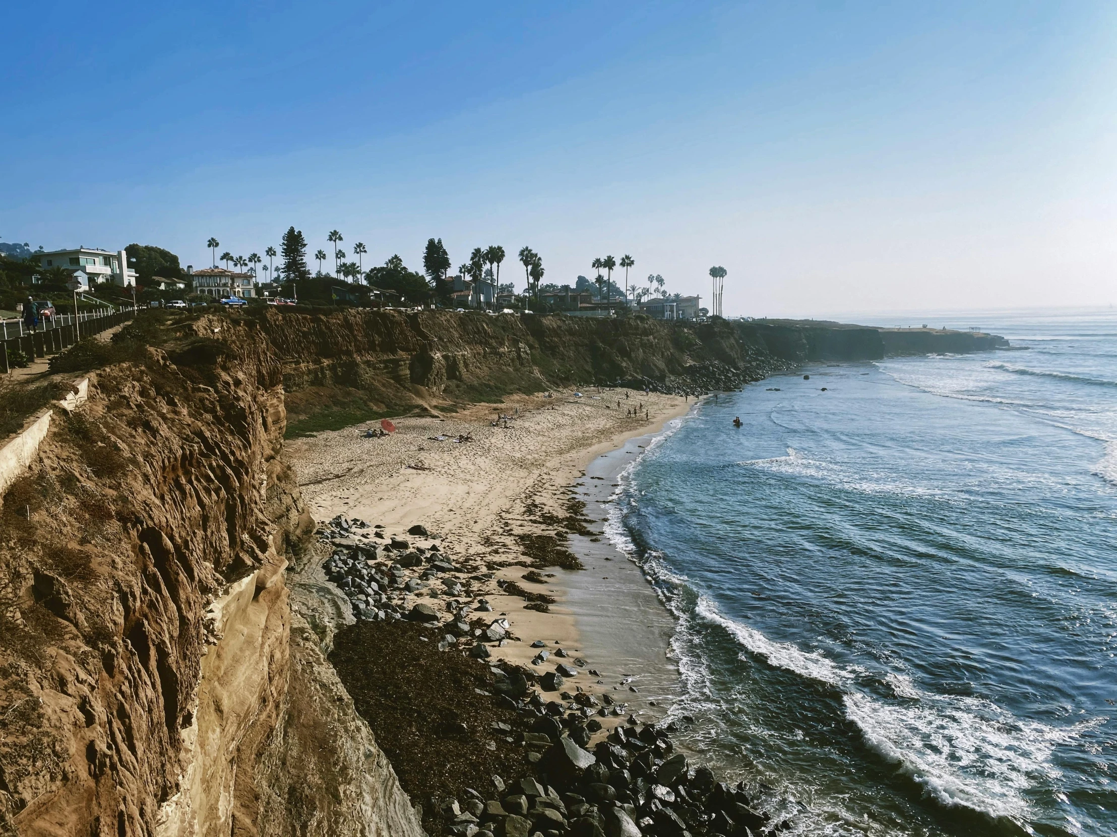 a man riding a skateboard down the side of a cliff, by Robbie Trevino, palm trees on the beach, erosion algorithm landscape, summer street near a beach, listing image