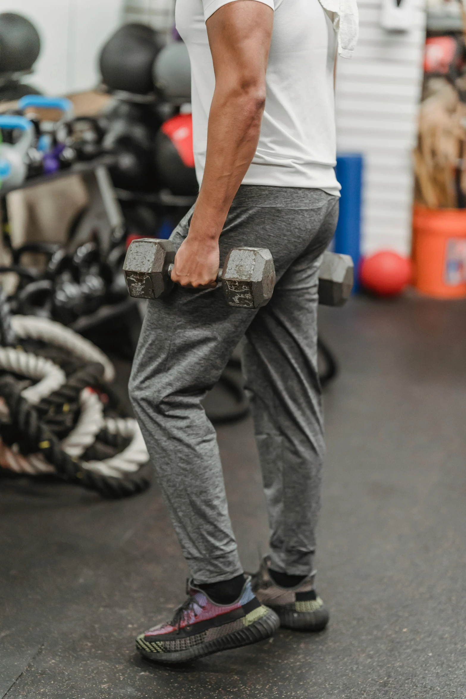 a man holding two dumbbells in a gym, by Jason Felix, wearing pants, profile image, breeches, grey