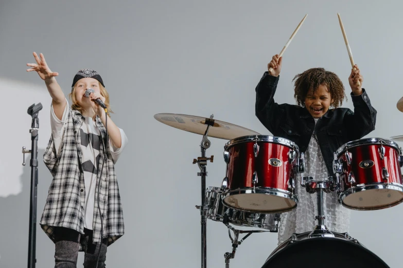 a group of people standing on top of a stage, by Nina Hamnett, pexels, antipodeans, playing drums, portrait willow smith, kids, on grey background