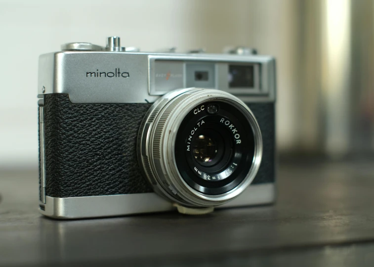 a camera sitting on top of a wooden table, a picture, minoru nomata, modern minimalist f 2 0 clean, front facing the camera, grey metal body