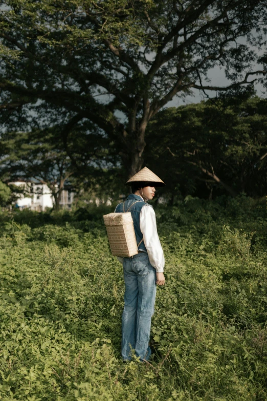 a man standing in a field holding a basket, an album cover, by Yosa Buson, unsplash, mingei, square backpack, 千 葉 雄 大, architect, handcrafted