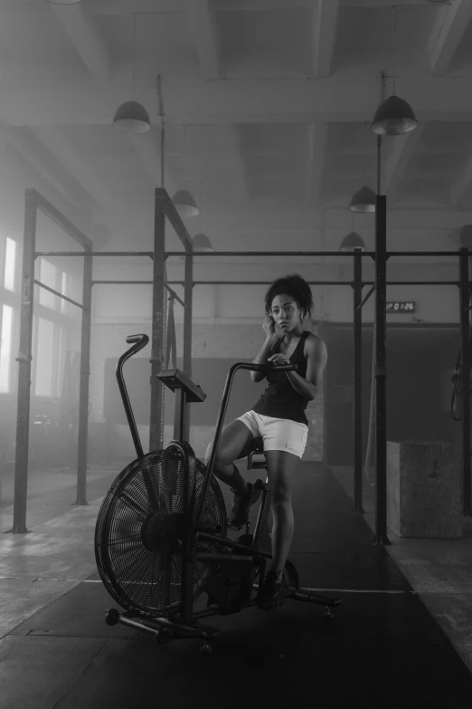 a woman standing next to a bike in a gym, a black and white photo, by Adam Marczyński, realism, summer morning, photo of a black woman, octane cgsociety, spinning