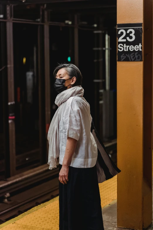 a woman standing on a subway platform wearing a face mask, by Andrew Stevovich, late summer evening, profile image, humans of new york style, white scarf