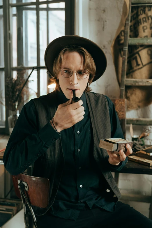 a man sitting at a table reading a book, a portrait, inspired by Johannes Mytens, trending on pexels, smoking a pipe, jamie campbell bower, wearing cylinder hat, cardistry