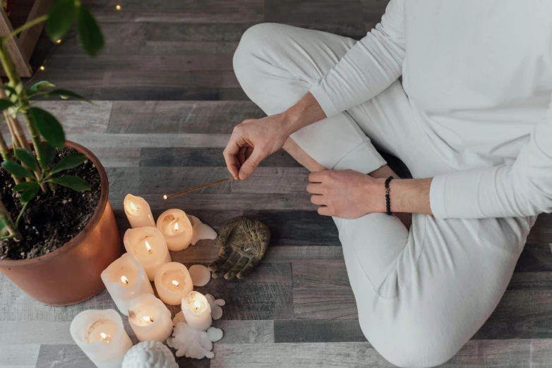 a man sitting on the floor next to a potted plant, trending on pexels, light and space, white candles dripping wax, kundalini energy, wooden magic wand, serpentine pose