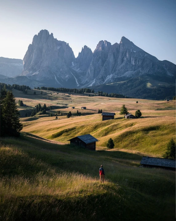 a person standing in a field with mountains in the background, pexels contest winner, renaissance, dolomites, nat geo, late afternoon, conde nast traveler photo