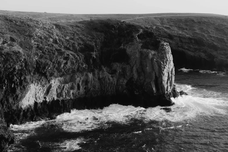 a black and white photo of a cliff near the ocean, 4 k photo, marsden, an extremely large cave, drone footage