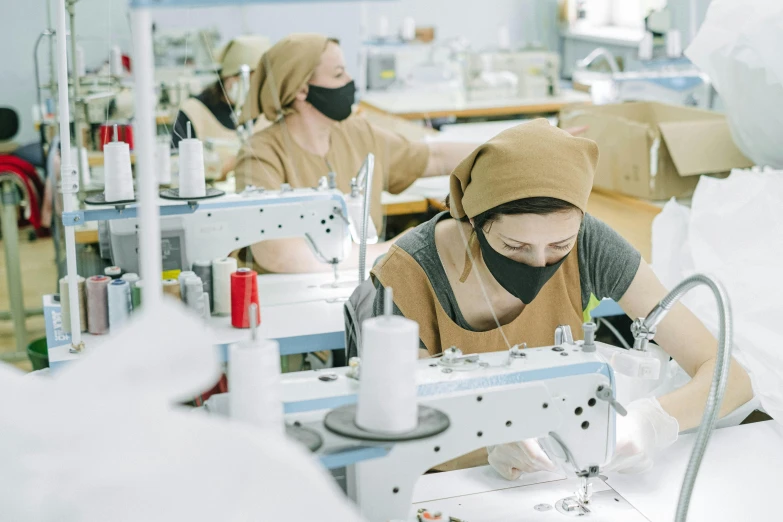 two women working on sewing machines in a factory, by Nicolette Macnamara, trending on pexels, renaissance, wearing facemask, avatar image, manuka, wearing hoods