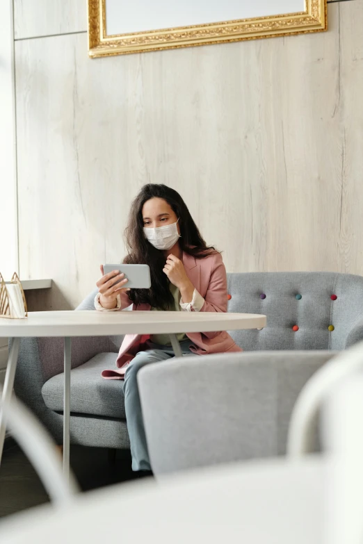 a woman sitting at a table using a cell phone, mask off, sitting in a lounge, grey, square