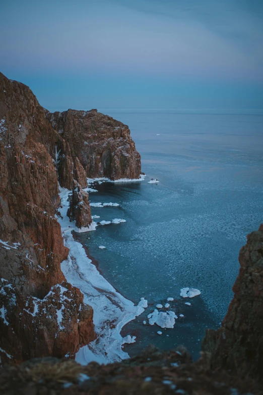 a large body of water next to a rocky cliff, inspired by Konstantin Vasilyev, pexels contest winner, frozen sea, dusk setting, red sea, high angle shot