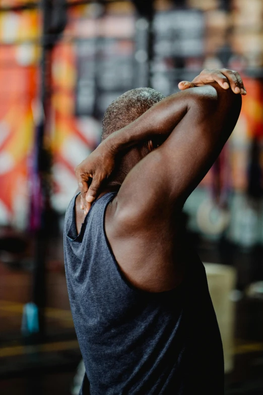 a man standing in front of a wall with graffiti on it, trending on pexels, in a gym, showing her shoulder from back, black human spine, pixeled stretching