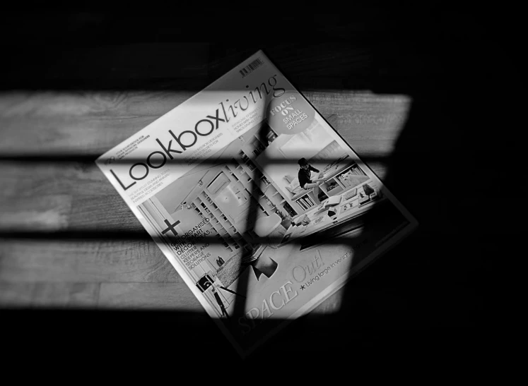 a newspaper sitting on top of a wooden bench, a black and white photo, inspired by László Moholy-Nagy, lowbrow, light rays and shadows, lockbox, cover magazine, softbox lighting