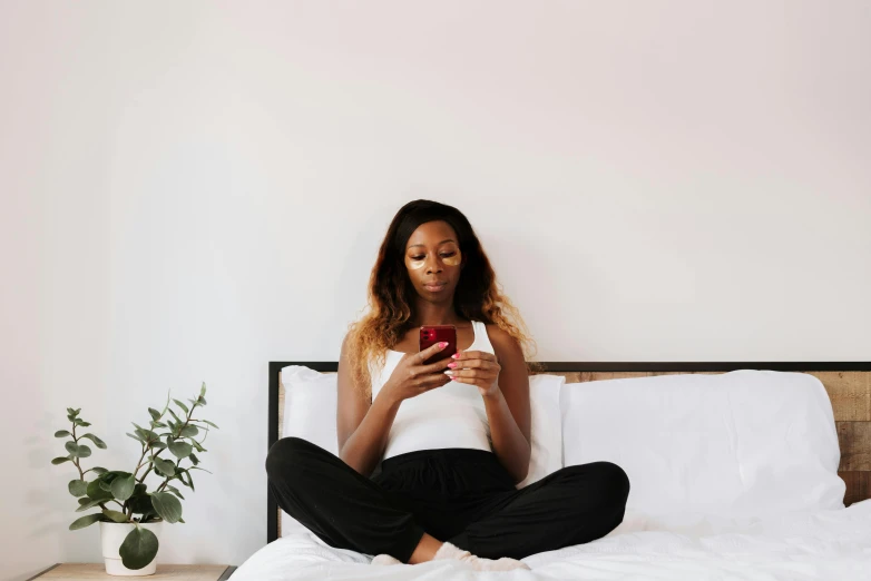 a woman sitting on a bed looking at her phone, trending on pexels, black girl, meditation pose, slightly red, slightly minimal