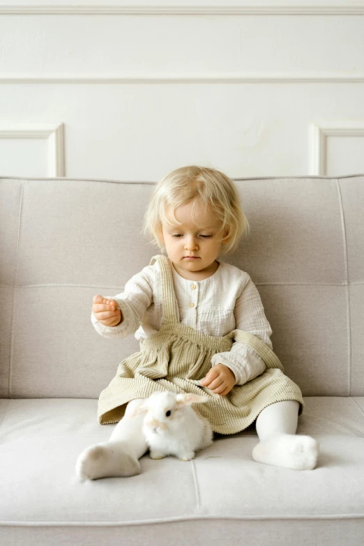 a little girl sitting on a couch with a stuffed animal, inspired by Elsa Beskow, pexels contest winner, ultrarealistic sweet bunny girl, white sleeves, toddler, snacks