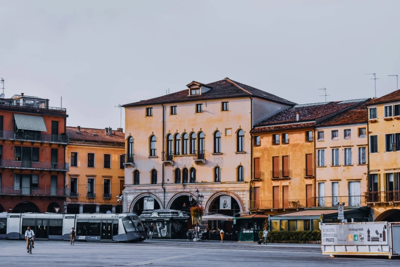 a group of buses driving down a street next to tall buildings, an album cover, inspired by Gaetano Sabatini, pexels contest winner, italian renaissance architecture, white marble buildings, profile image, village square