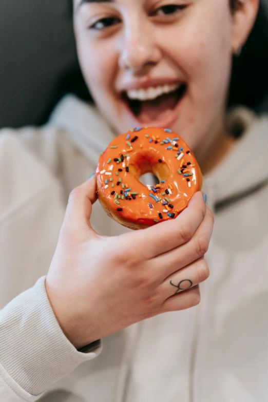 a woman holding a donut with sprinkles on it, by Julia Pishtar, trending on pexels, antipodeans, black and orange, made of baked beans, teenage boy, excited