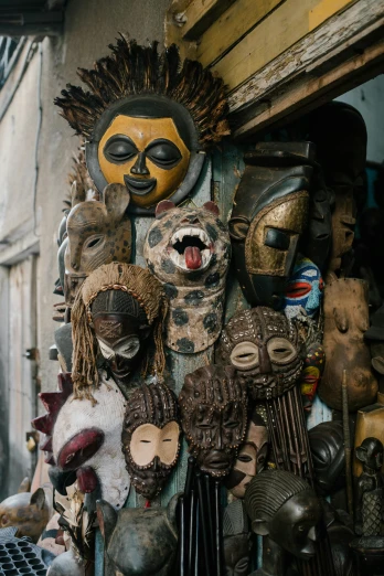 a group of masks hanging from the side of a building, afrofuturism, crafts and souvenirs, animal - shaped statue, cabinet of curiosities, shot with sony alpha