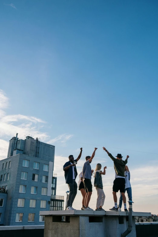 a group of people standing on top of a building, by Niko Henrichon, unsplash, happening, waving and smiling, blue sky, rooftop party, oceanside