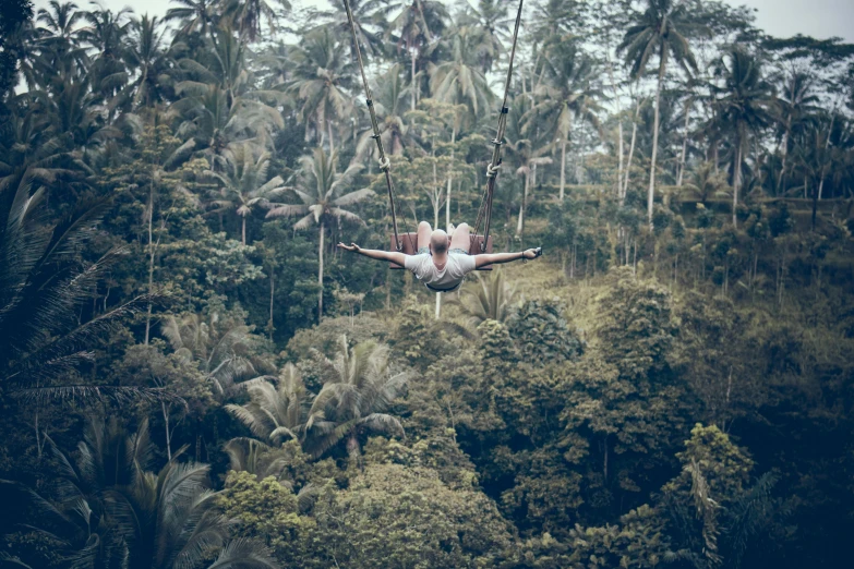 a man flying through the air over a lush green forest, a portrait, by Emma Andijewska, pexels contest winner, sumatraism, slim aarons, 🦩🪐🐞👩🏻🦳, brown, vintage photo