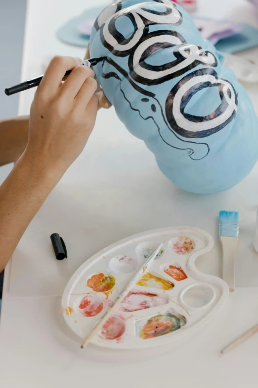 a woman painting a balloon with the word boo on it, process art, ceramic looking face, lightblue acrylic paintdrip tar, promo image, tabletop