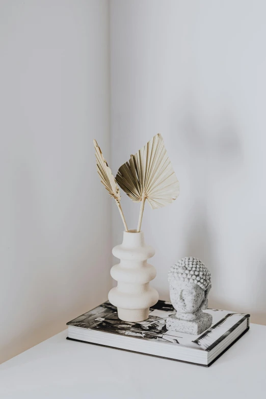 a white table topped with a vase filled with flowers, an abstract sculpture, trending on unsplash, minimalism, palm body, textured base ; product photos, spines and towers, boho neutral colors