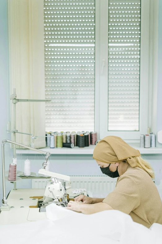 a woman working on a sewing machine in a room, surgical gear, muslim, thumbnail, beige