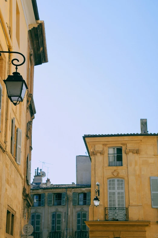 a group of people walking down a street next to tall buildings, neoclassicism, lourmarin, street lamp, yellows, patina