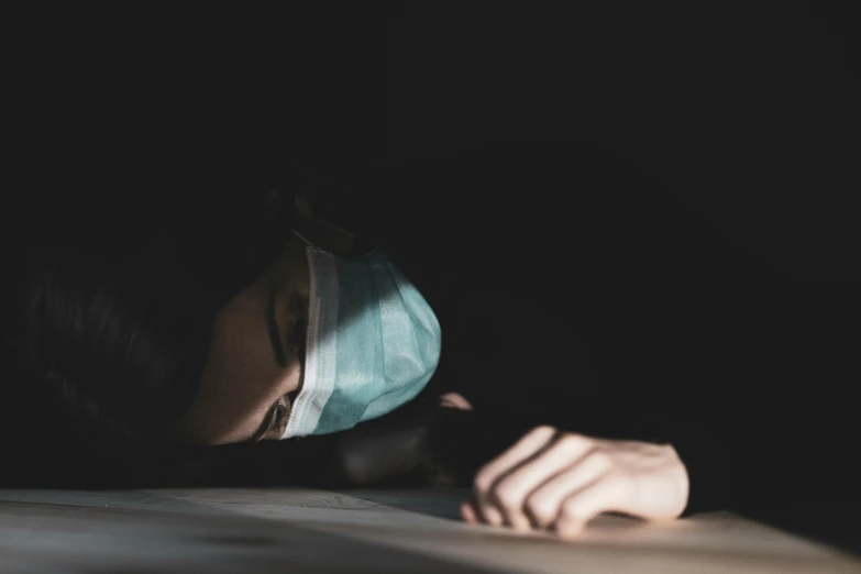 a close up of a person wearing a face mask, a picture, pexels, hyperrealism, lying down, sad scene, healthcare worker, dark scene with dim light