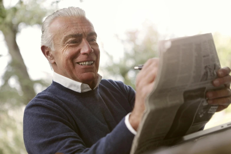 a man sitting at a table reading a newspaper, a photo, gray haired, looking happy, regular build, colour photograph