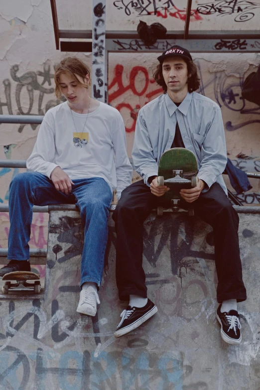 a couple of men sitting on top of a skateboard ramp, a picture, by Winona Nelson, renaissance, frank dillane, loosely cropped, scowl, low quality photo