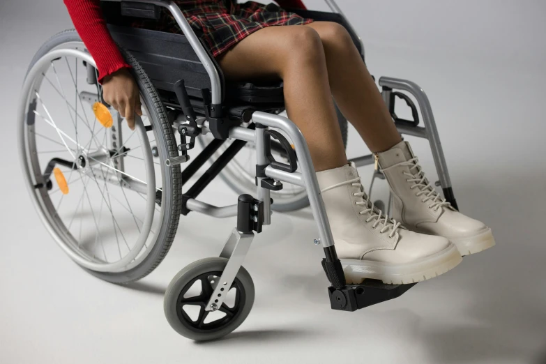 a woman is sitting in a wheel chair, trending on pexels, hurufiyya, heavy-duty boots, on grey background, white mechanical details, multi-part