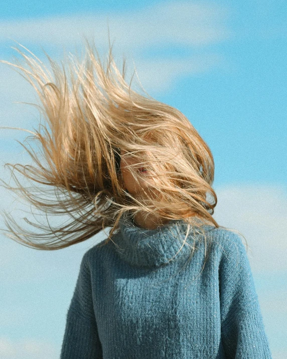 a woman with her hair blowing in the wind, by Rachel Reckitt, trending on unsplash, blue sweater, human head with blonde hair, whirling, light blue sky