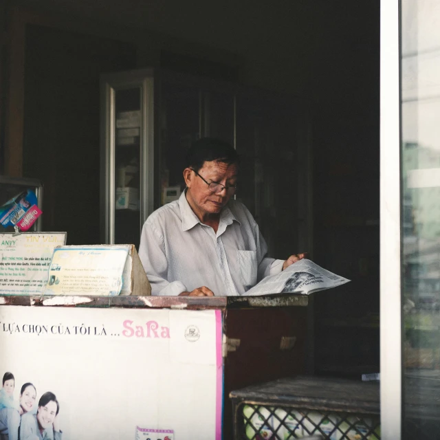 a man that is standing in the doorway of a building, a photocopy, unsplash, vietnamese woman, reading glasses, at the counter, compassionate