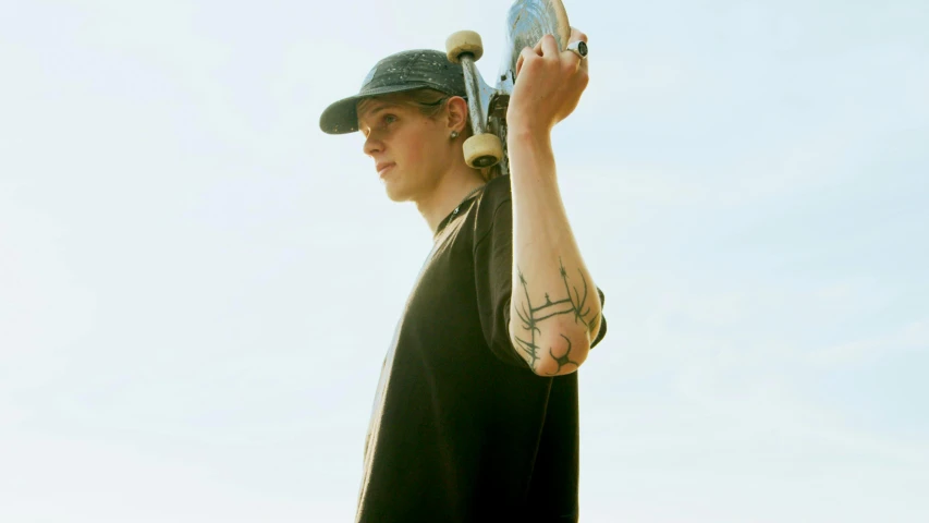 a man holding a skateboard in his hand, a tattoo, inspired by Seb McKinnon, unsplash, realism, wearing a baseball cap backwards, jamie campbell bower, an epic non - binary model, holding a bell