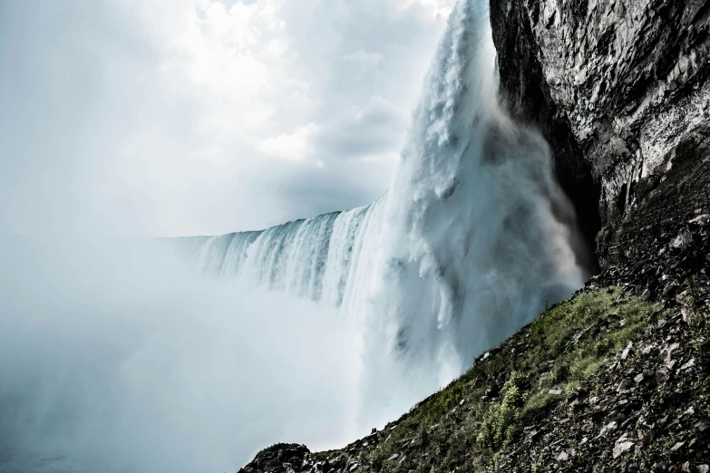 a man standing on top of a cliff next to a waterfall, an album cover, by Jesper Knudsen, pexels contest winner, hurufiyya, niagara falls, youtube thumbnail, whale fall, hyperdetailed photo