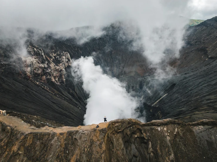 a group of people standing on top of a mountain, by Andrew Geddes, pexels contest winner, sumatraism, looking down at a massive crater, a person standing in front of a, grey, an explosion