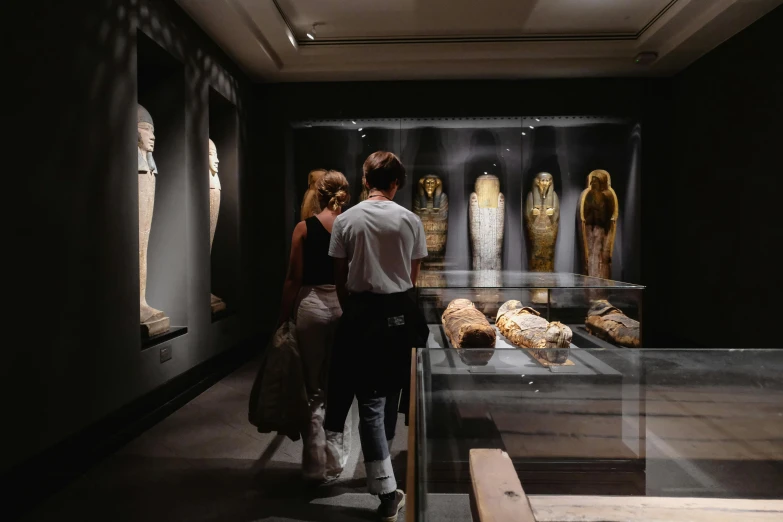 a couple of people standing in front of a display case, egyptian art, by Tom Wänerstrand, pexels, visual art, inside the sepulchre, summer evening, mummy, the photo shows a large