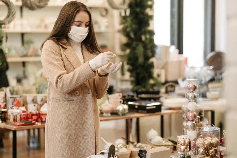 a woman wearing a face mask in a store, by Emma Andijewska, pexels, happening, decorations, avatar image, holding flask in hand, seasonal