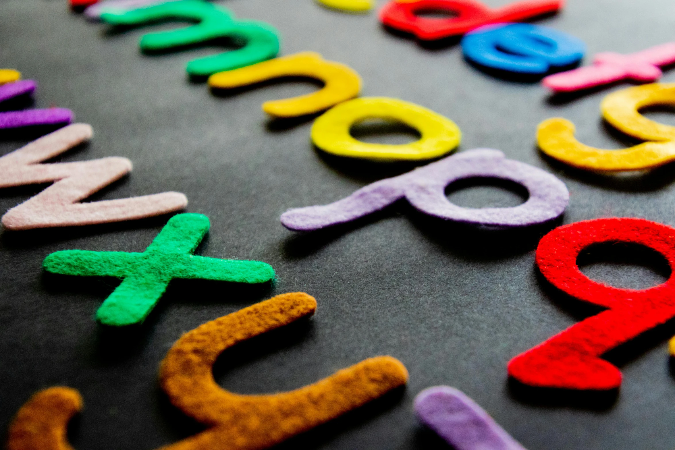 a close up of colorful wooden letters on a black surface, by Anna Findlay, pexels, needle felting, motion graphics, schools, educational