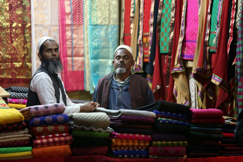 a couple of men sitting next to each other, hurufiyya, fabrics and textiles, people shopping, thumbnail, islamic